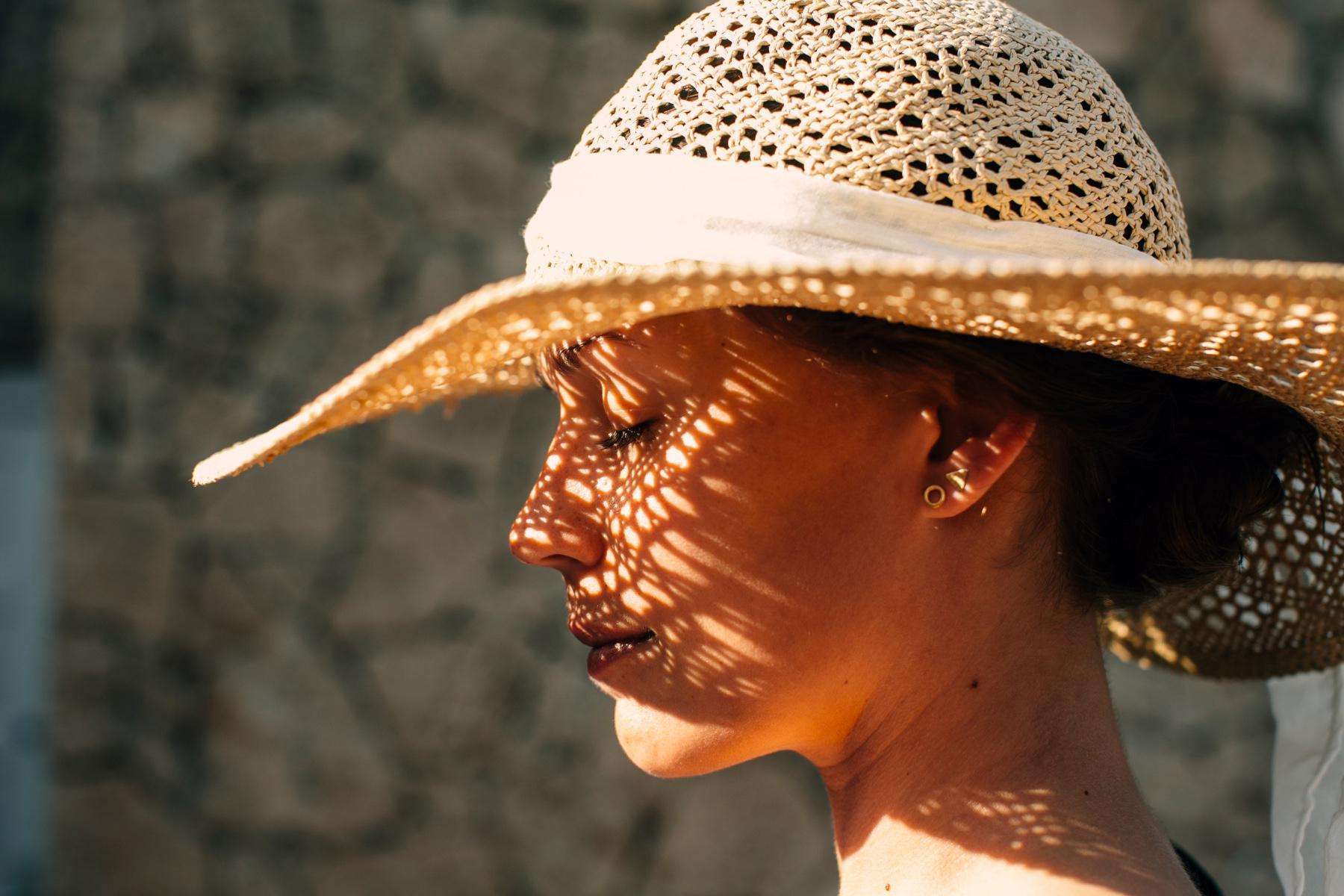 Close-up of a woman from the side wearing a sunhat that is casting a shadow on her face.