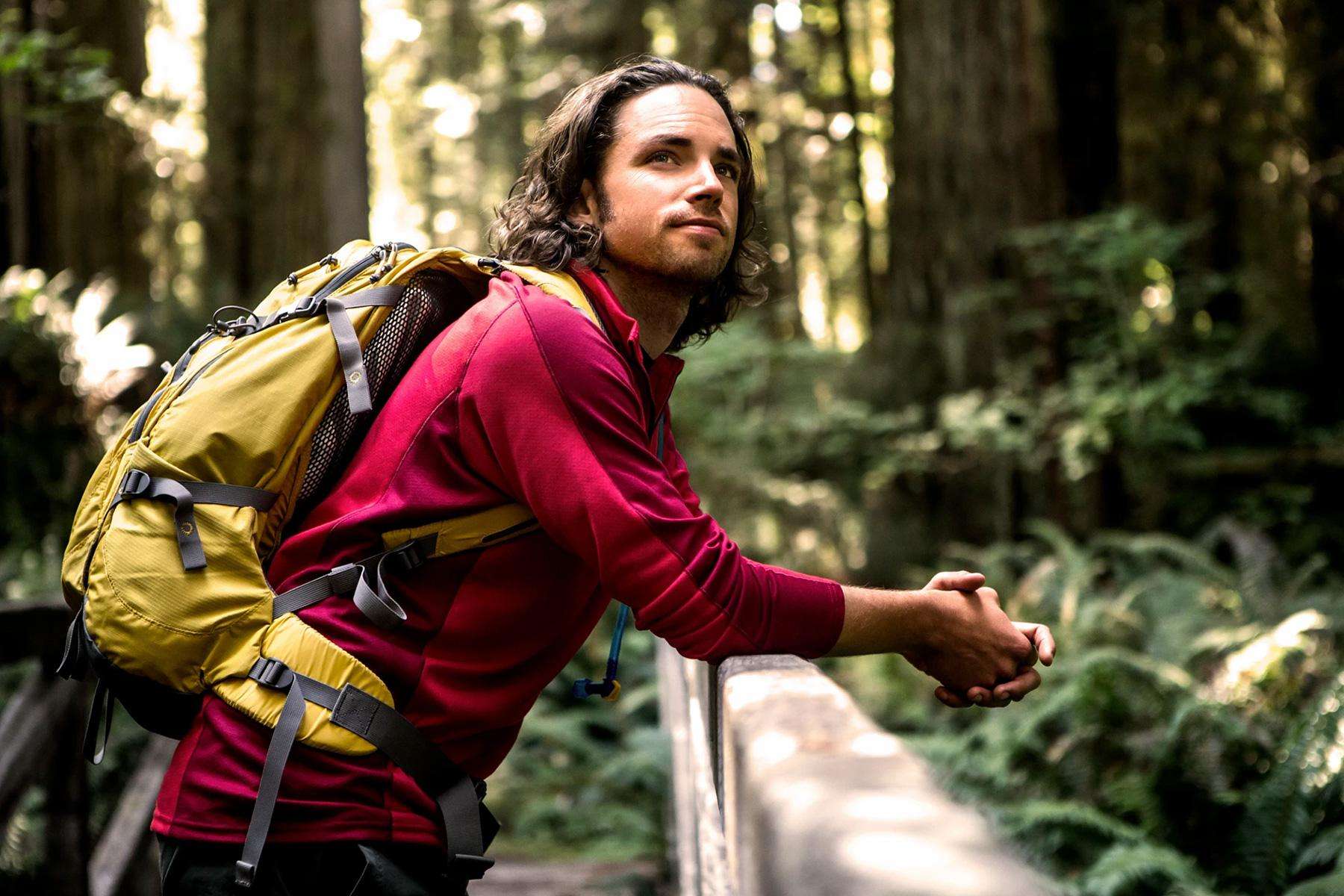 Man leaning on railing of bridge while hiking in a green forest.