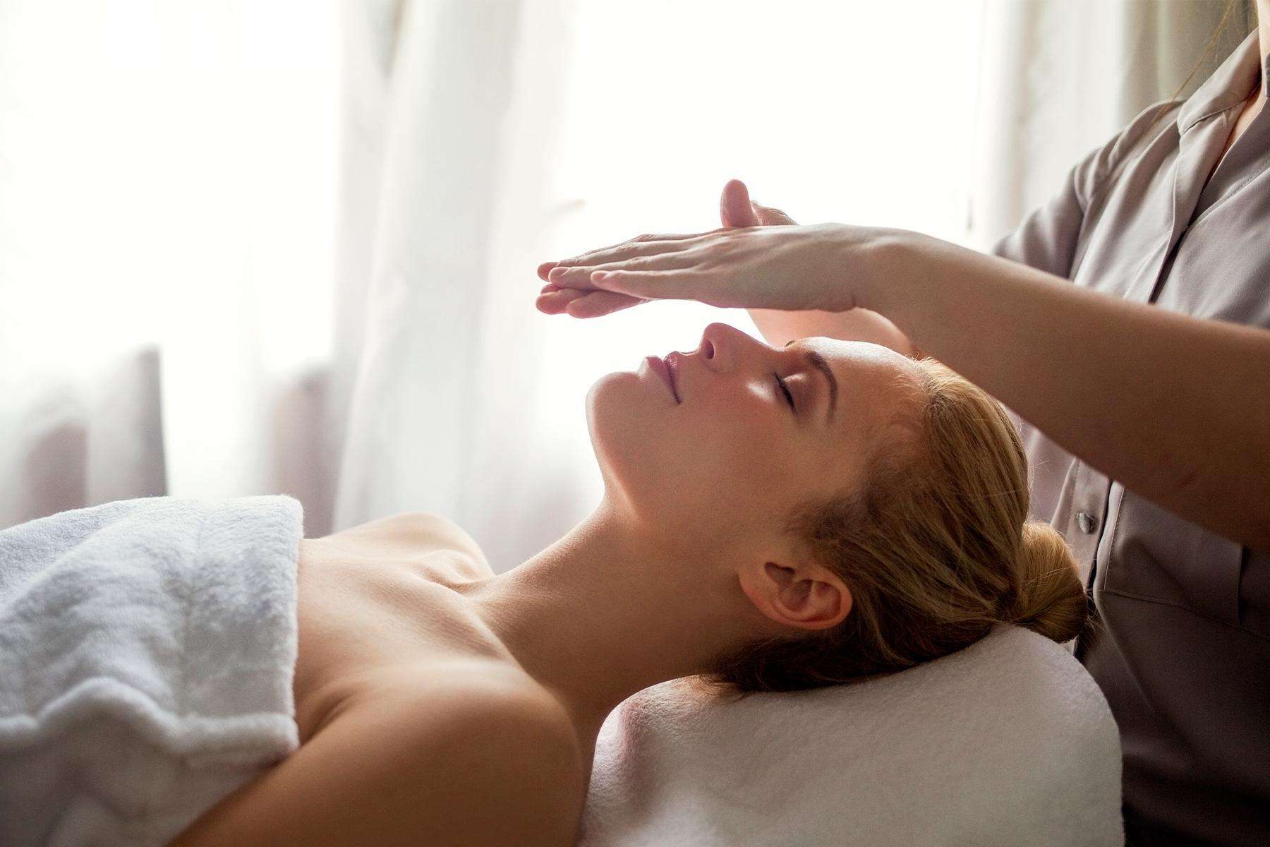 Woman laying on massage table with practitioner's hands above her face during a healing energy treatment.
