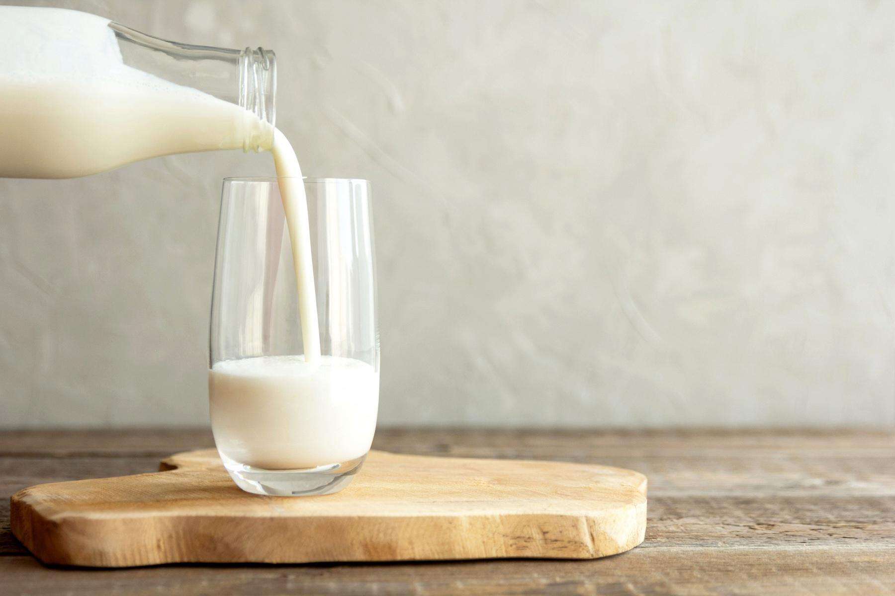 Milk being poured from glass bottle to glass cup.