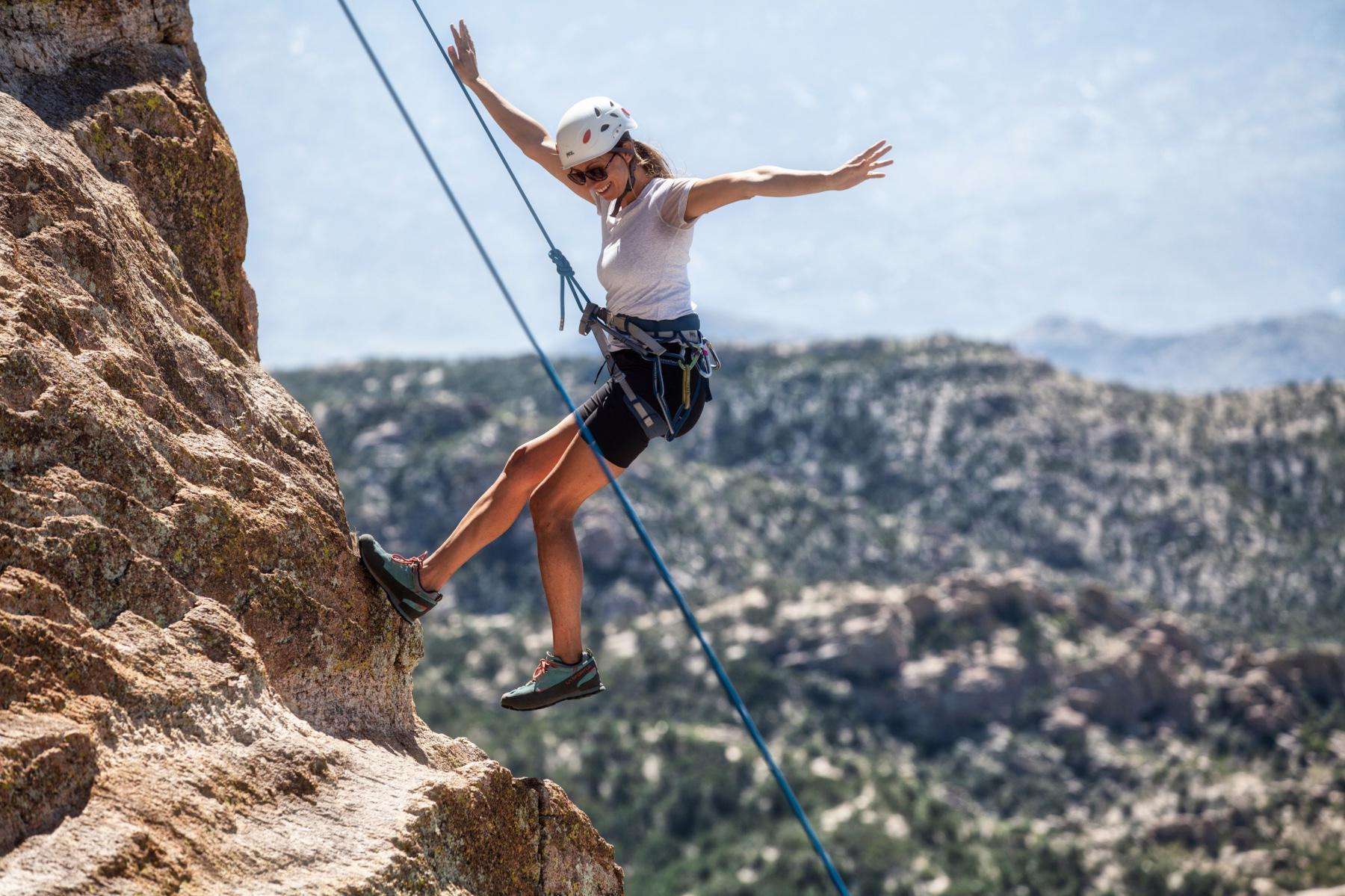 woman on side of rock face while rock climbing smiling while coming down