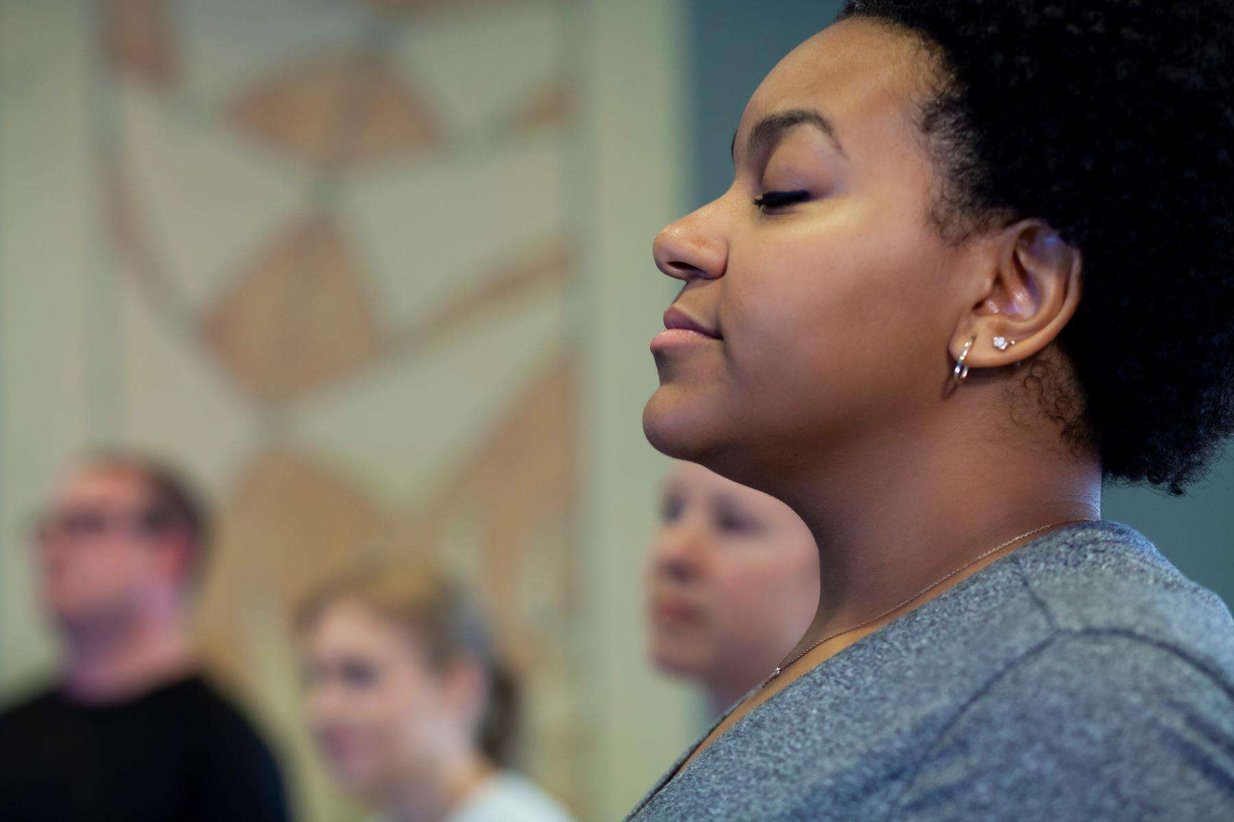 A close-up of a woman's face in a group meditation class.