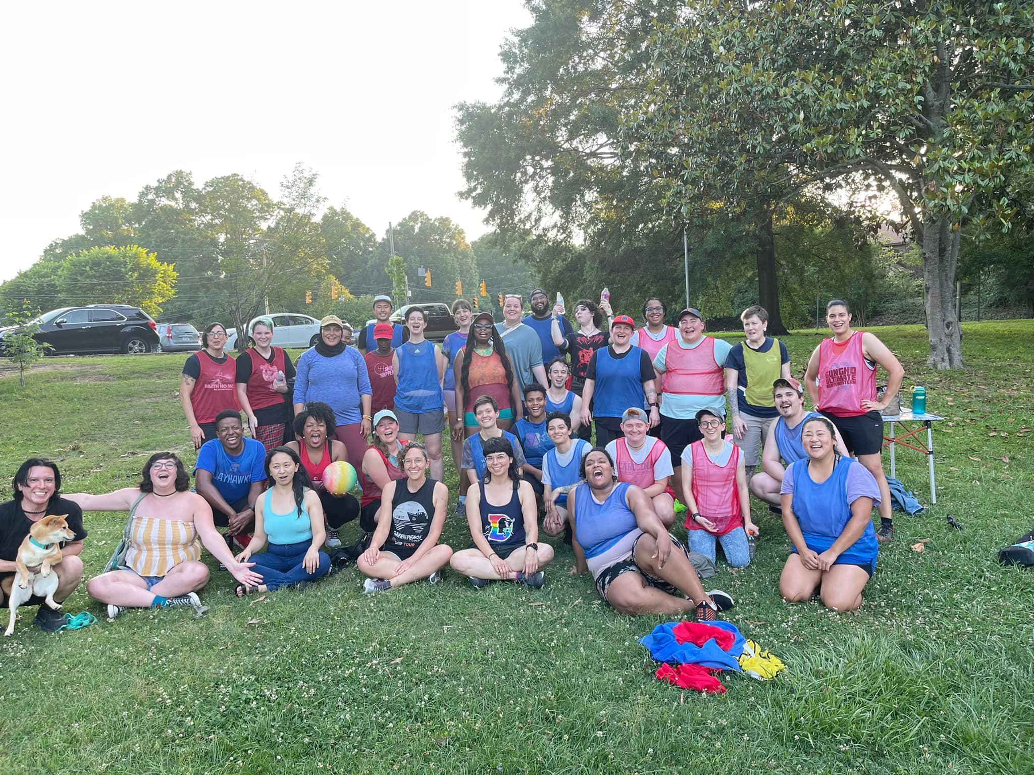A group of people wearing different colored jerseys posing together after a kickball game.