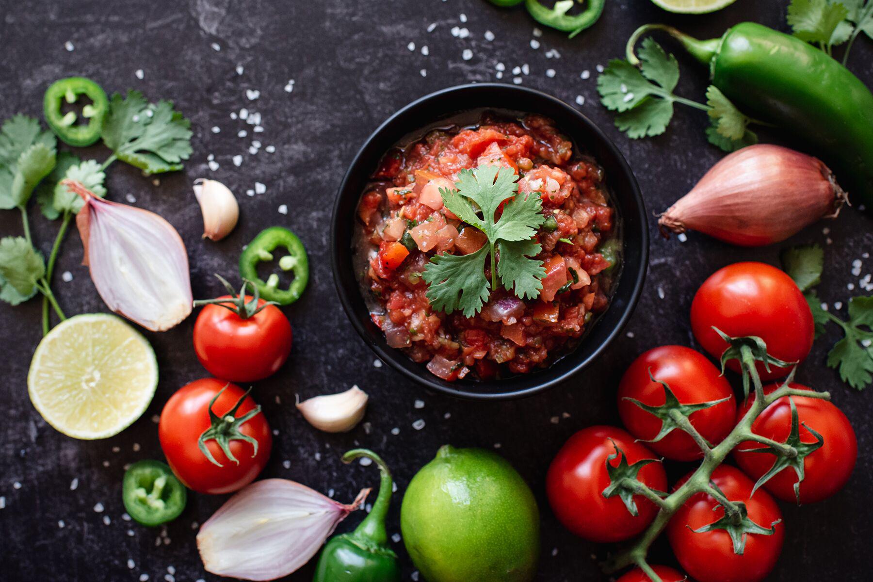 A bowl of salsa surrounded by a spread of ingredients