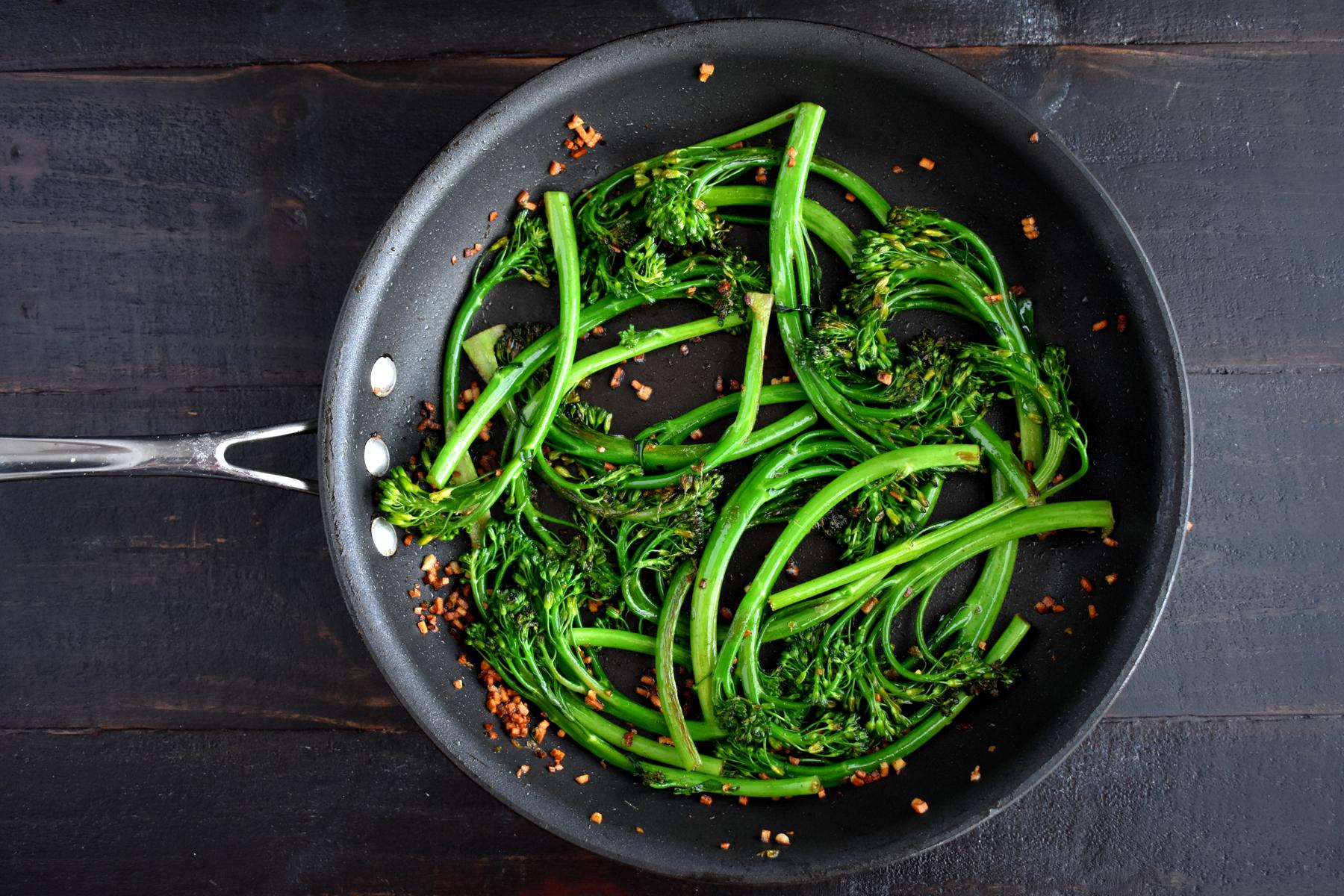 Overhead view of broccolini in black bowl.