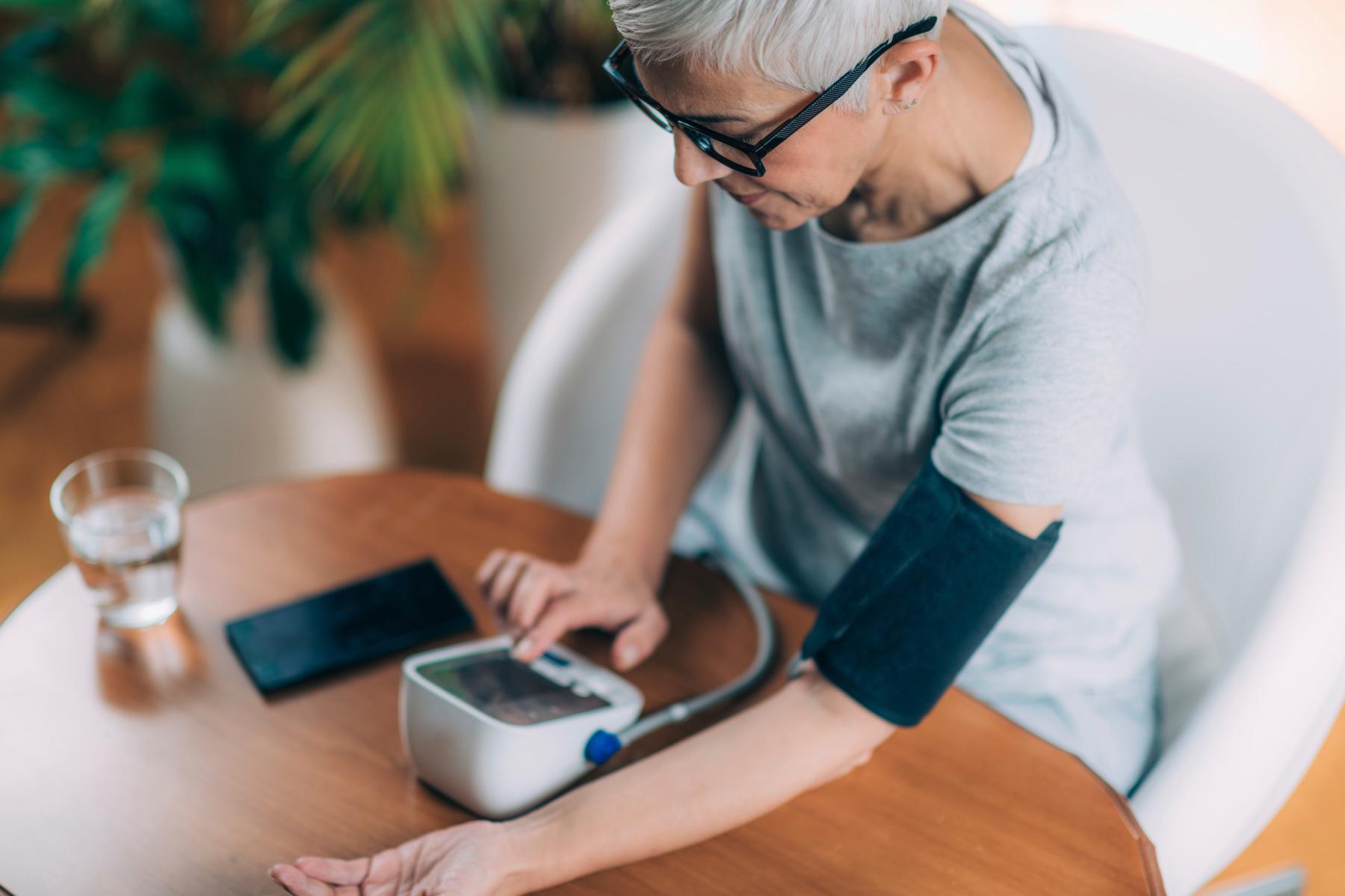 Woman sitting at table checking blood pressure.