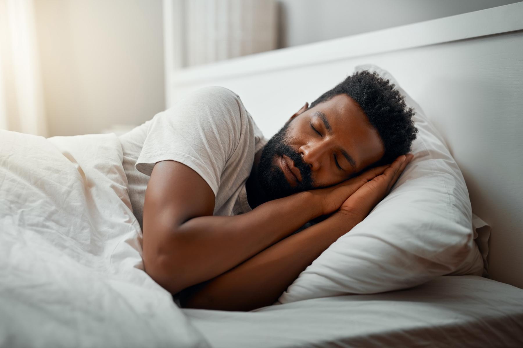 Man laying on his side in a bed with hands tucked up under the side of face.
