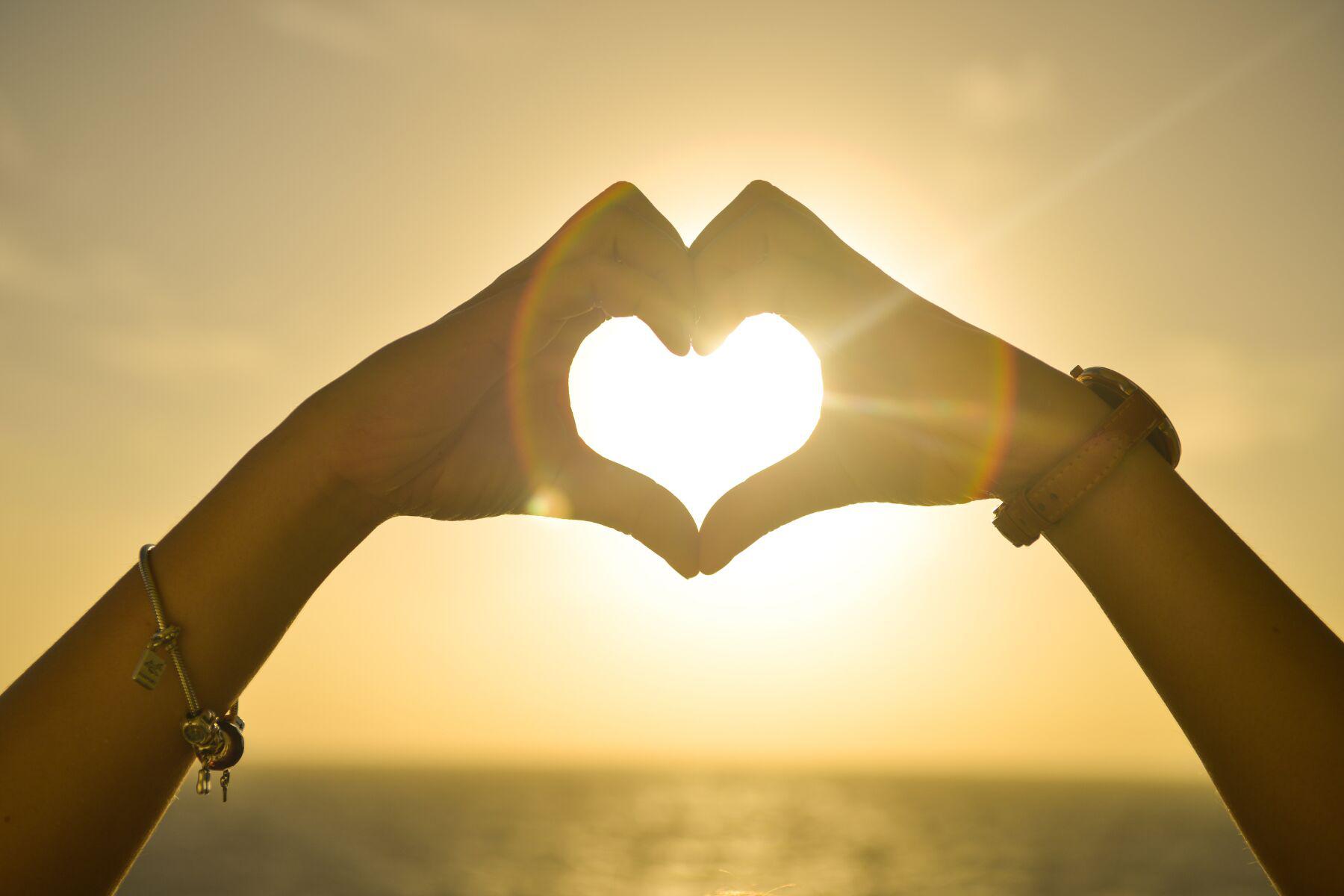 Hands making heart shape against sun