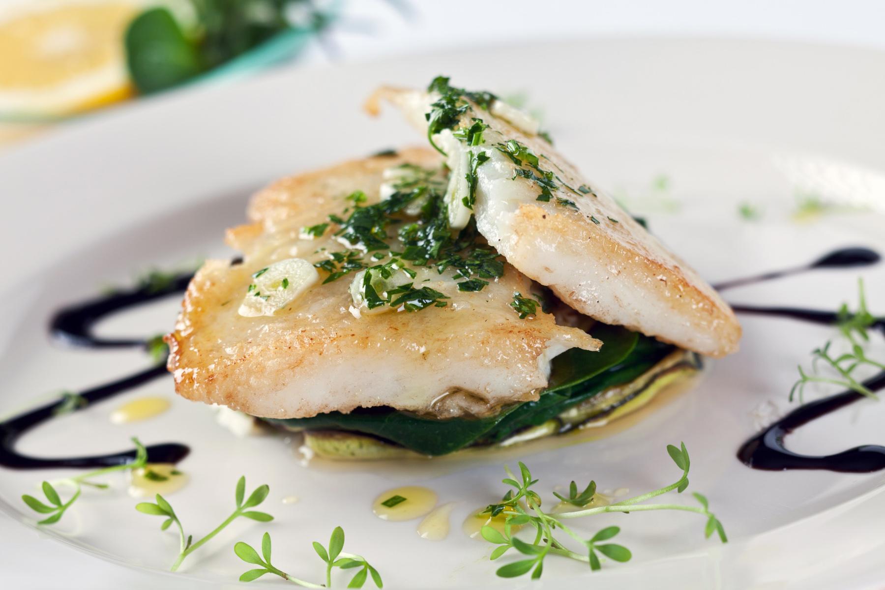 Cooked sole on plate with sauce drizzled around it.