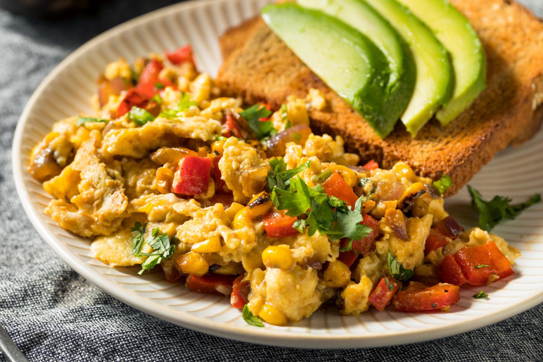 A plate of scrambled eggs with sliced avocado on the side.