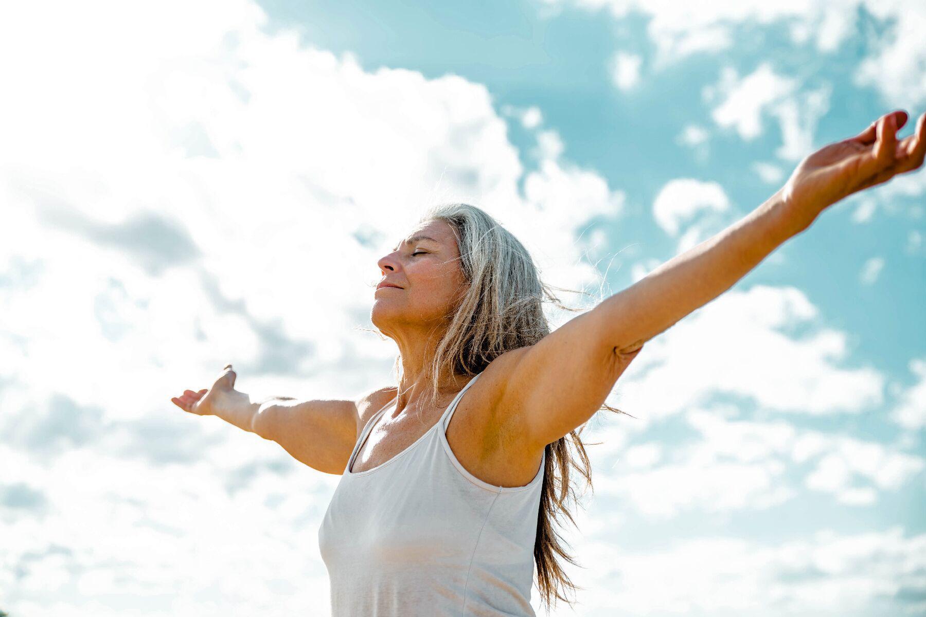 An older woman spreading her arms under a blue sky