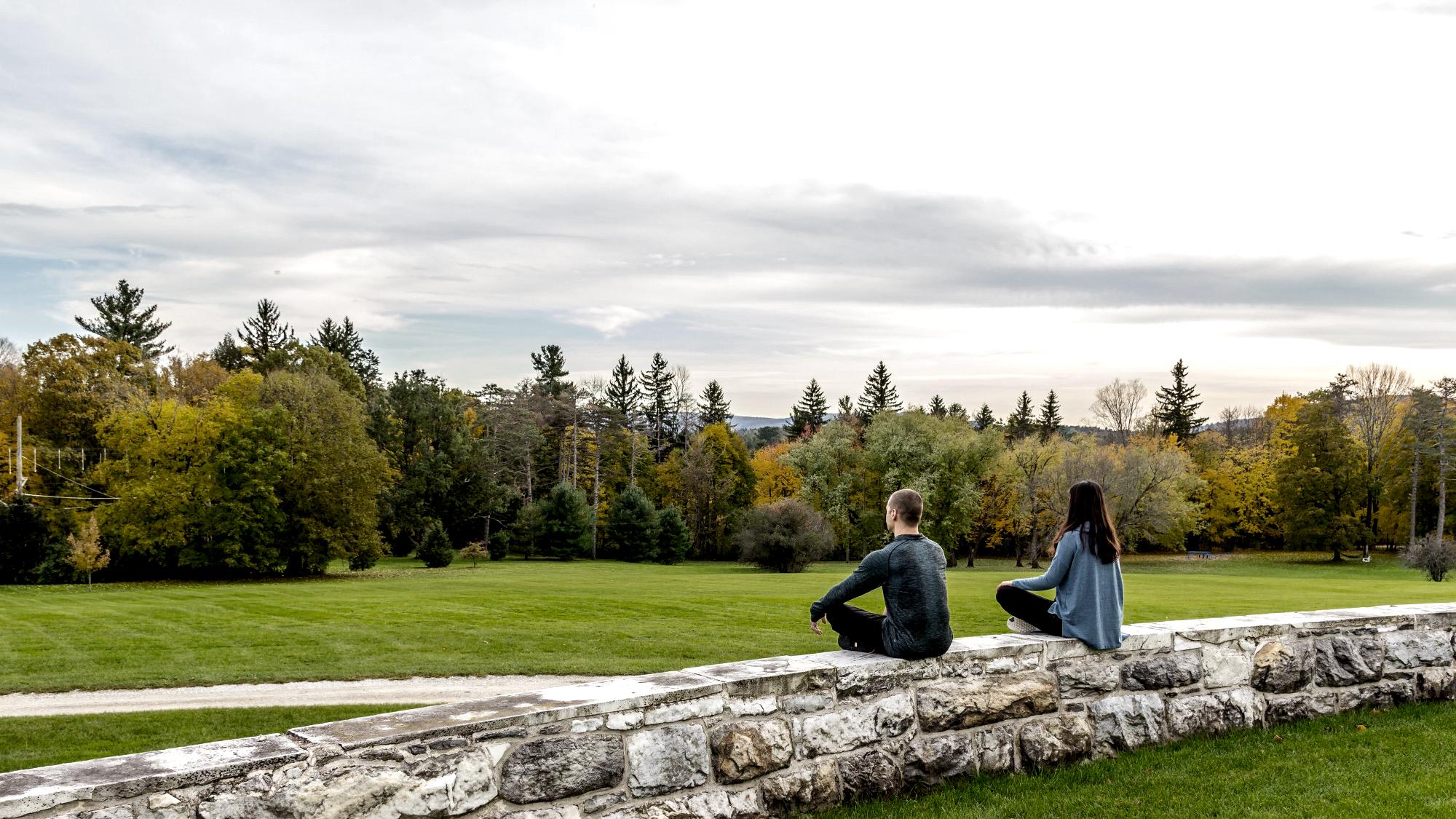 Couple in seated practice on wall overlooking great lawn.