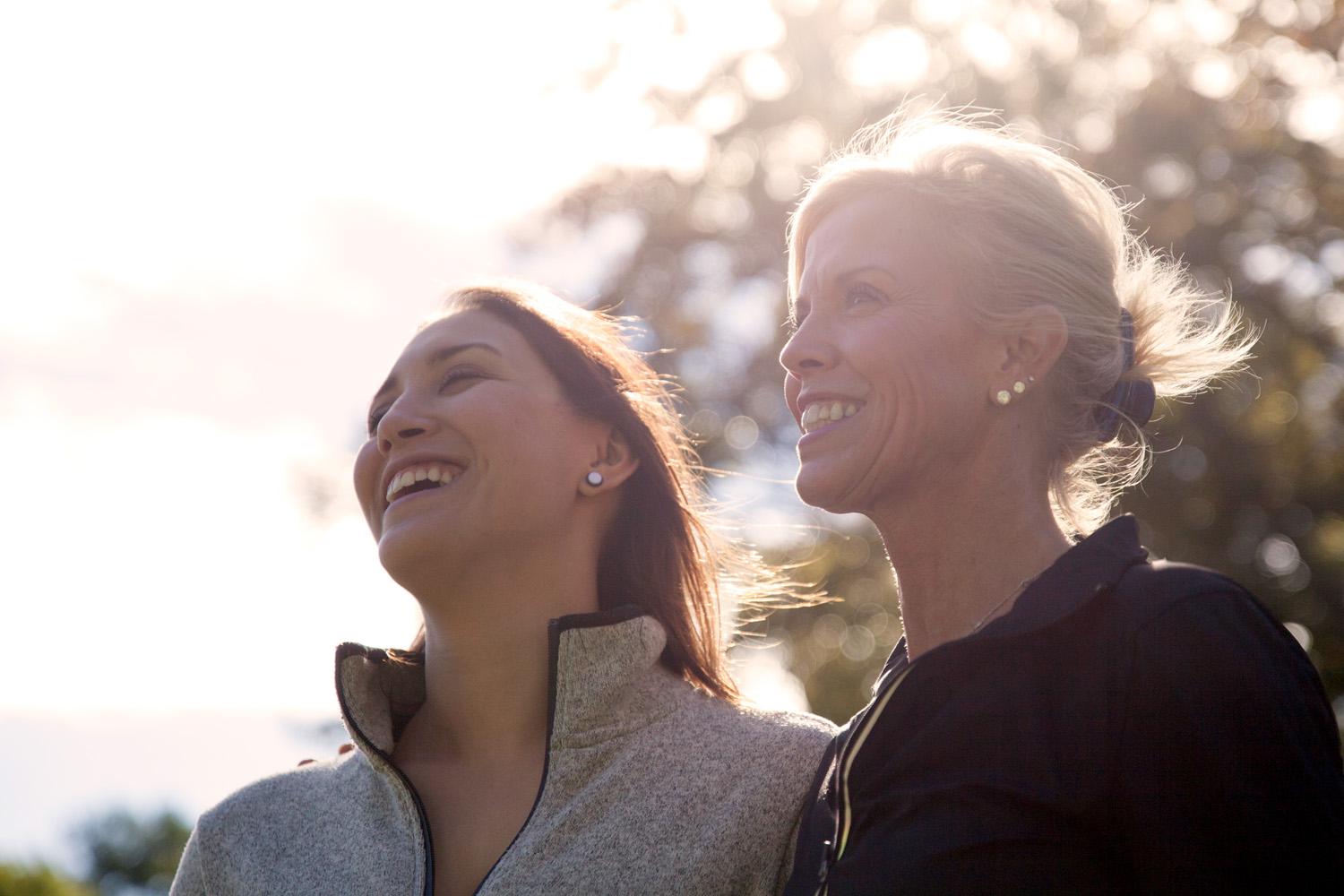A mother and daughter smiling outdoors in the sun