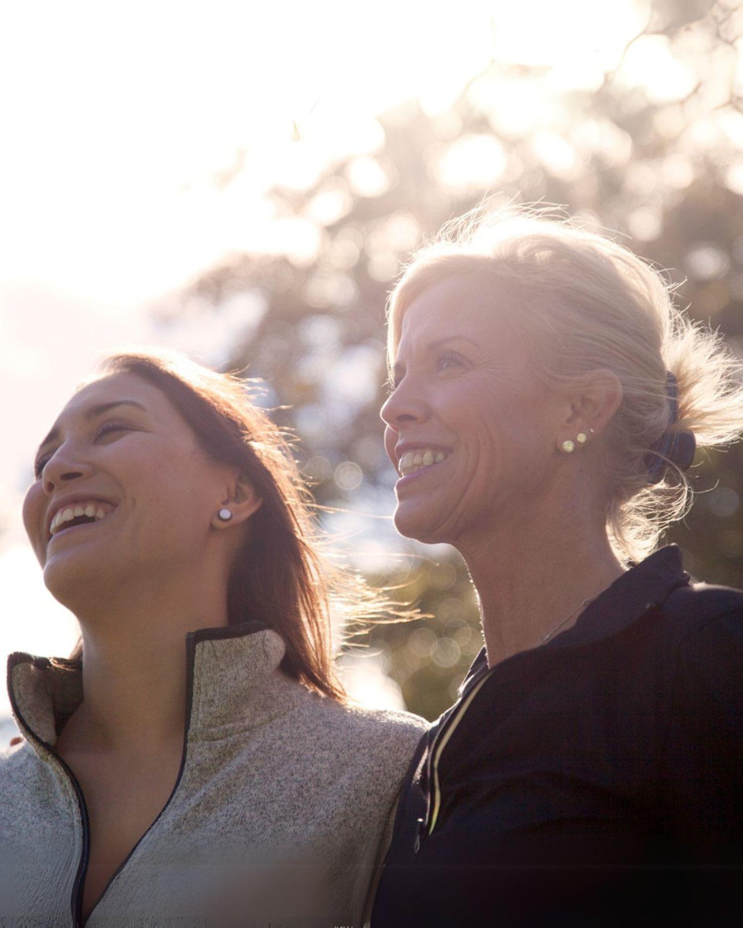 A mother and daughter smiling outdoors in the sun