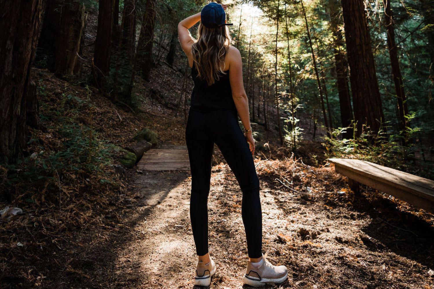 A woman standing in the forest looking up at the trees.