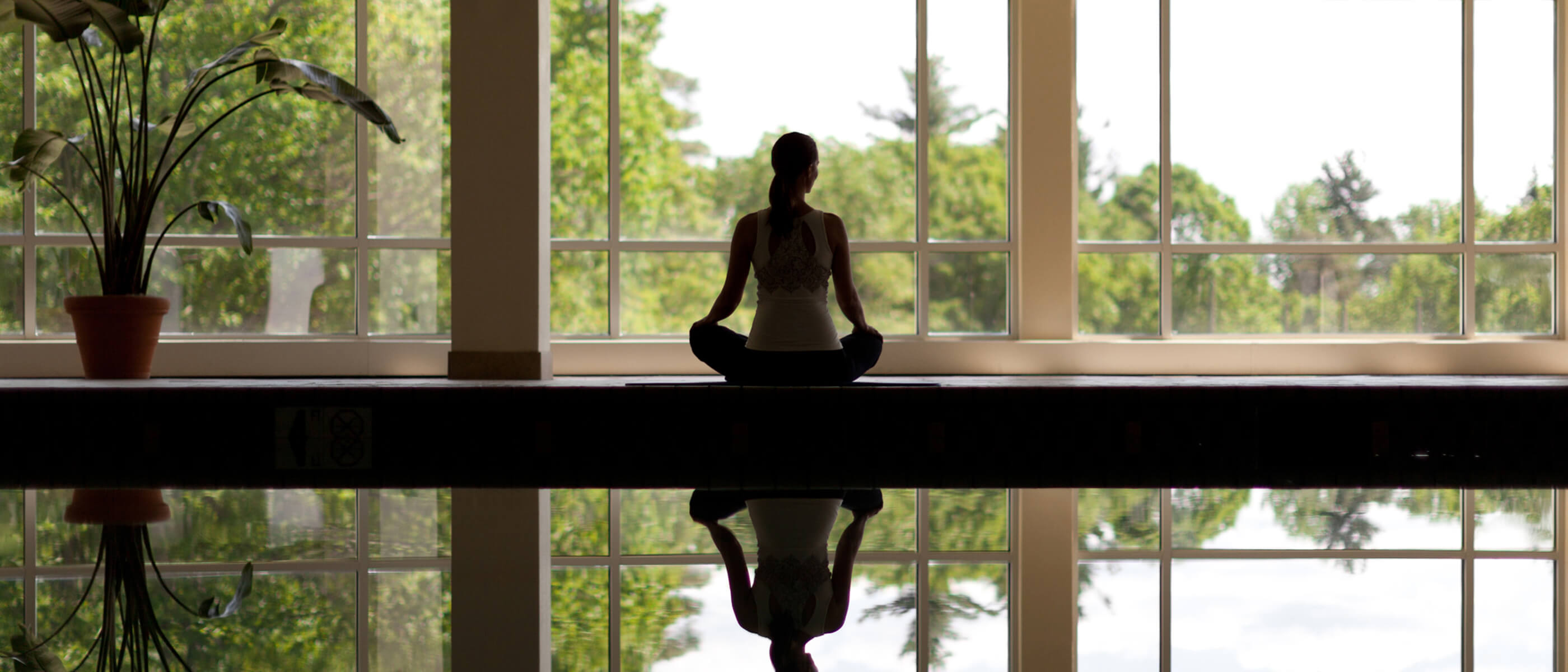 A woman sitting next to an indoor swimming pool meditating