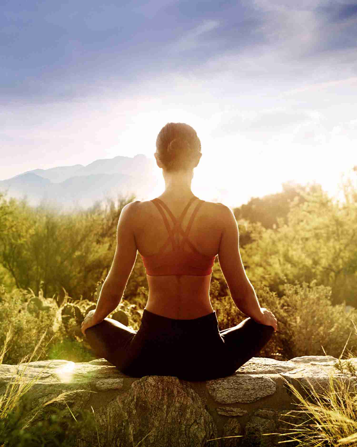 A woman sitting on a wall at sunrise meditating