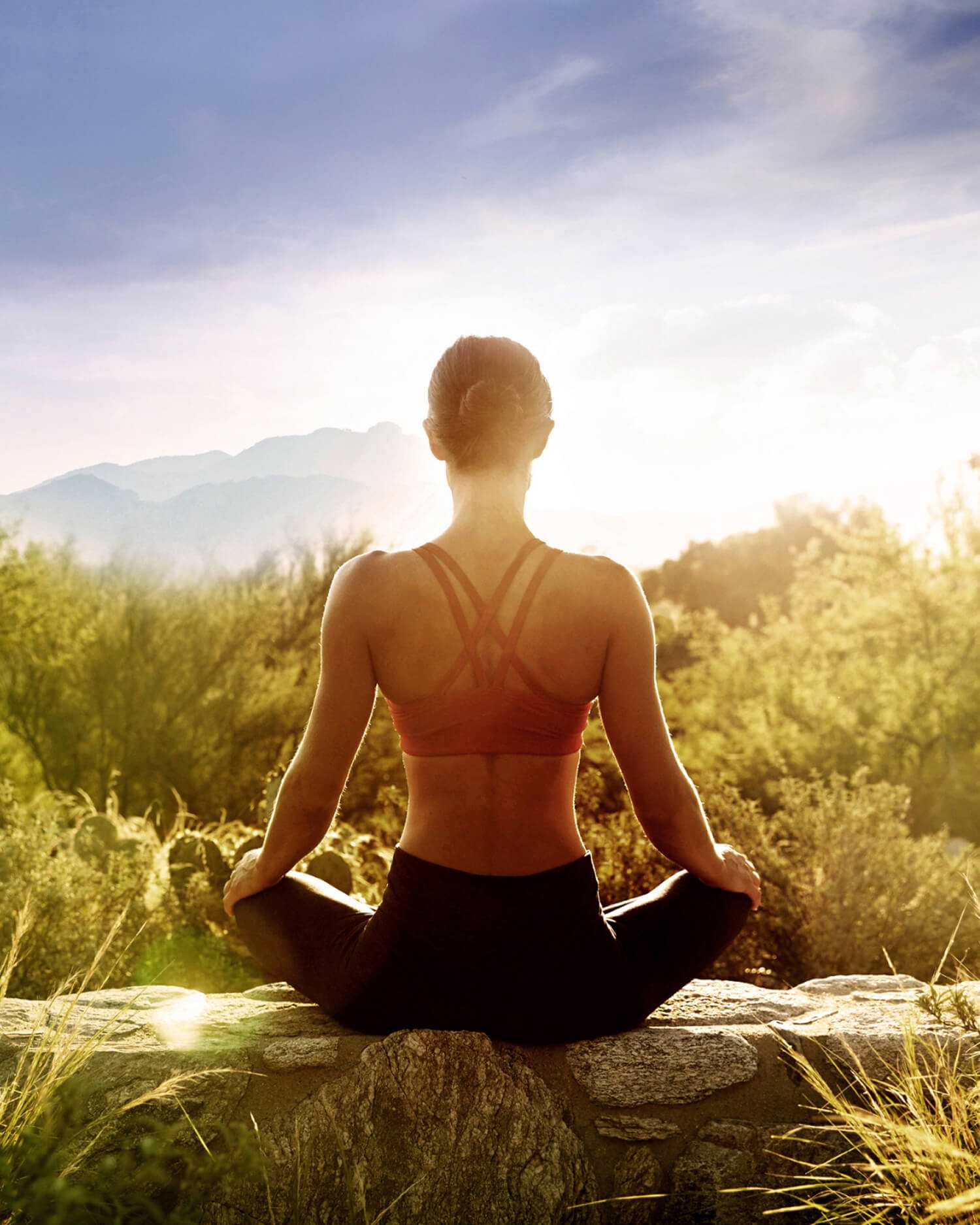 A woman sitting on a wall at sunrise meditating