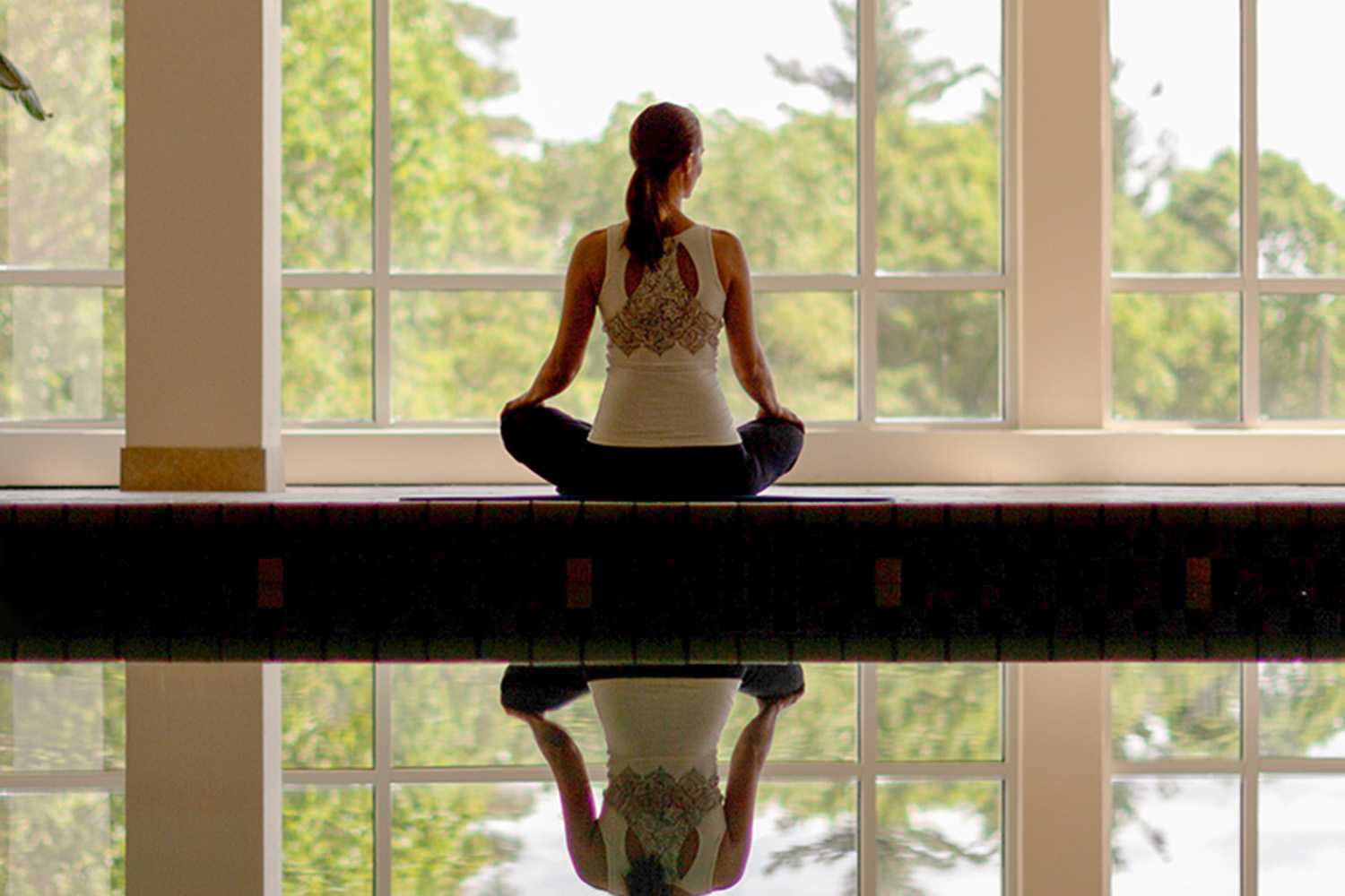 woman meditating in front of large windows