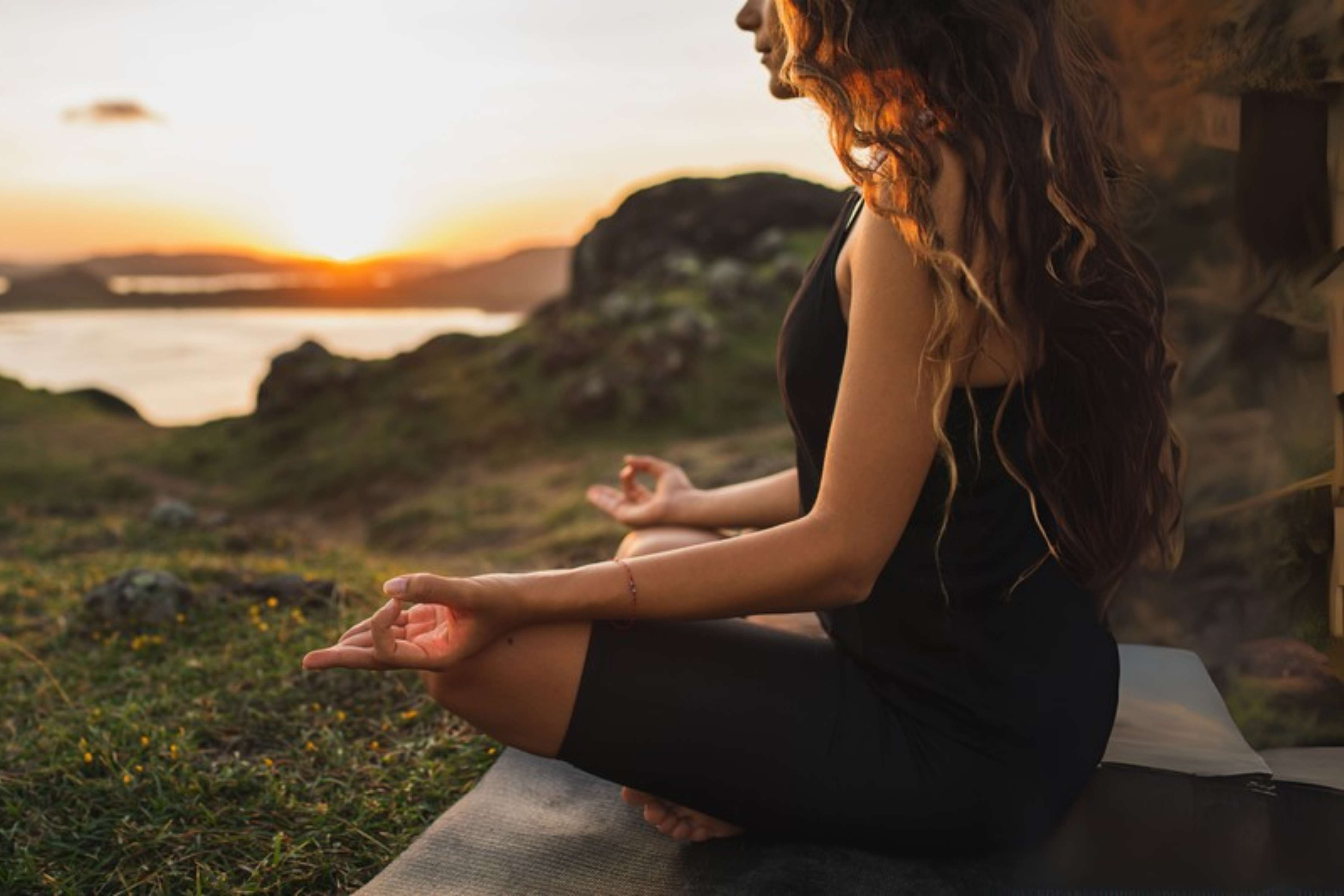 A woman meditating on a hill overlooking a lake