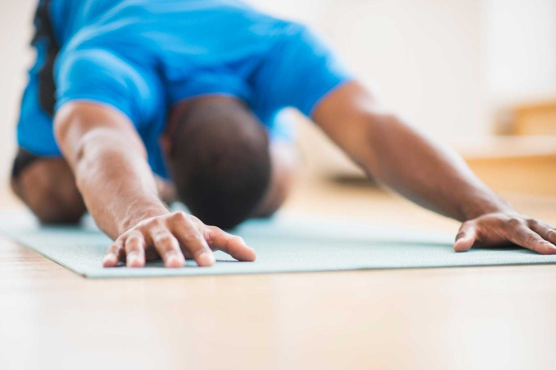 Man on yoga mat in child's pose position.